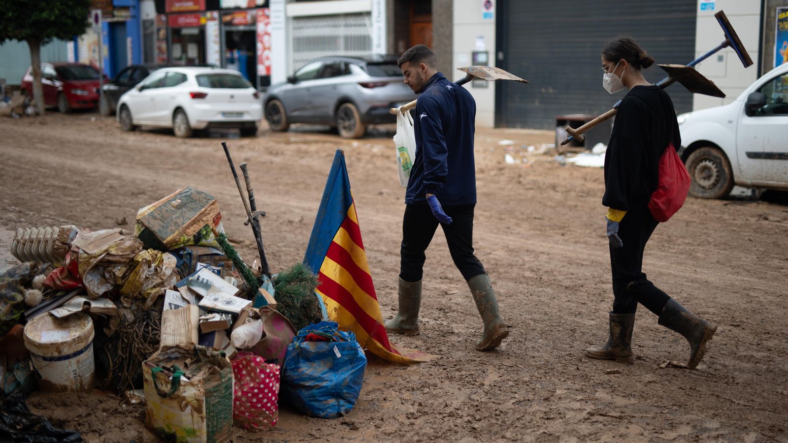 Dos persones amb pales observen una bandera de la Comunitat Valenciana mentre passen per un carrer de Benetússer este dilluns