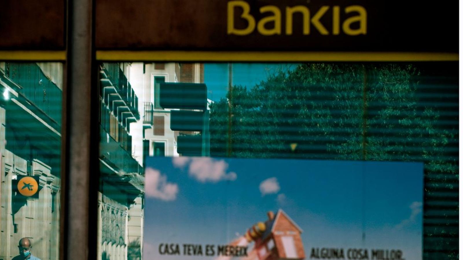 Vista d'una oficina de Bankia i una altra de CaixaBank reflectida en el cristall, a l'Hospitalet (Barcelona)