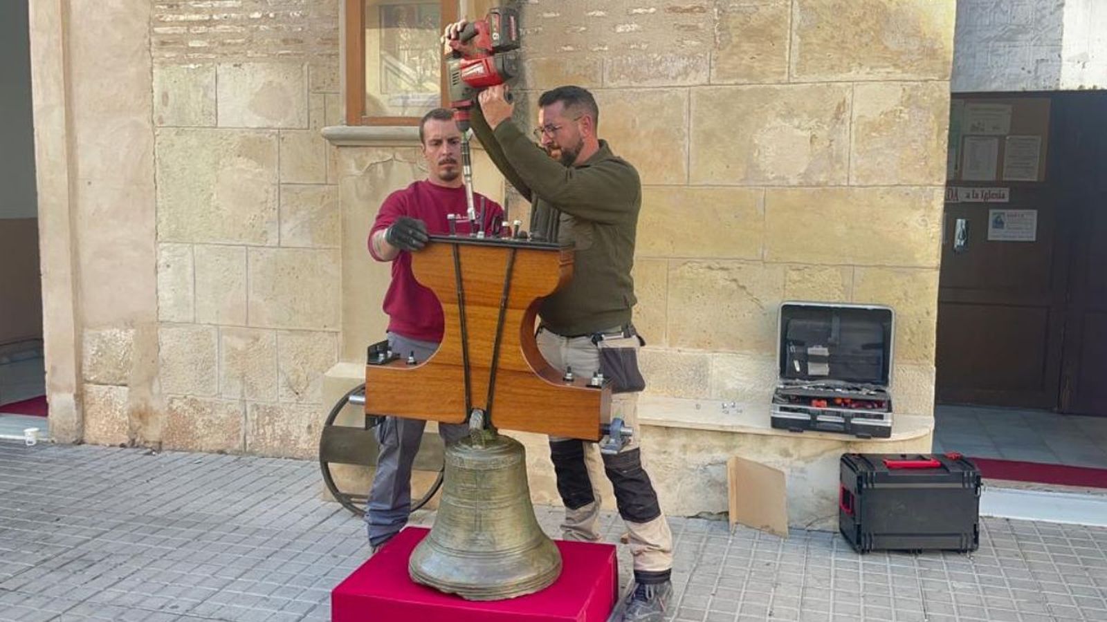 Els operaris treballen en ajustar la campana abans de tornar a pujar-la a la façana del campanari