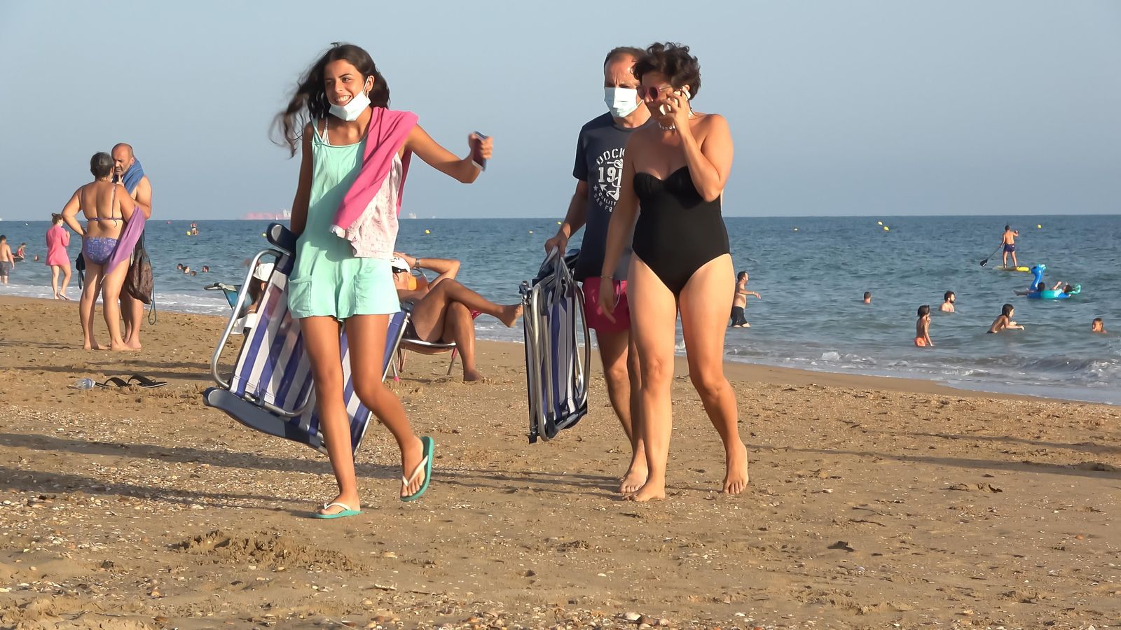 Un grup de persones camina per la platja amb mascareta