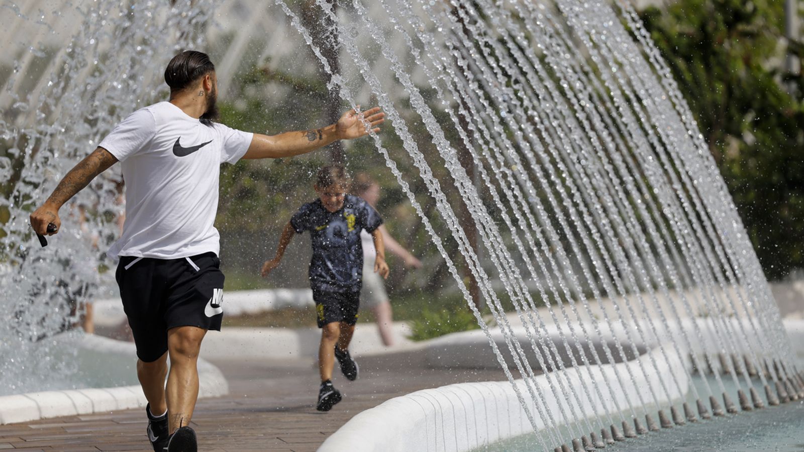 Un pare i el fill juguen amb unes fonts a València, en plena onada de calor