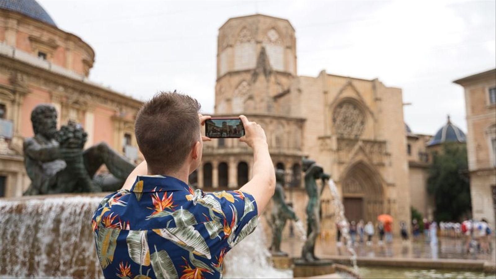 Un turista fa una foto a la plaça de la Mare de Déu de València Un turista fa una foto a la plaça de la Mare de Déu de València