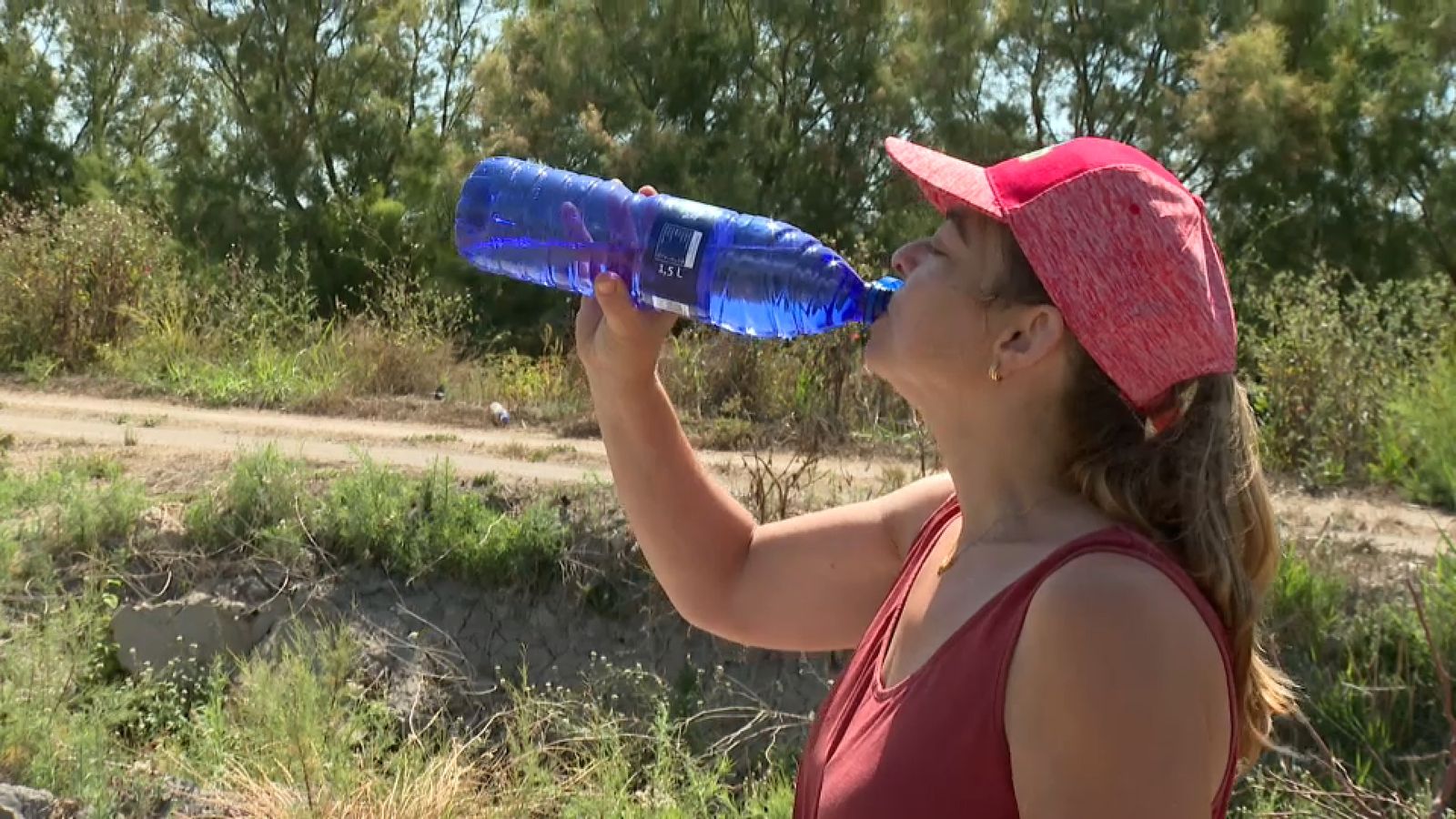 Una dona beu aigua en un entorn natural amb molta calor