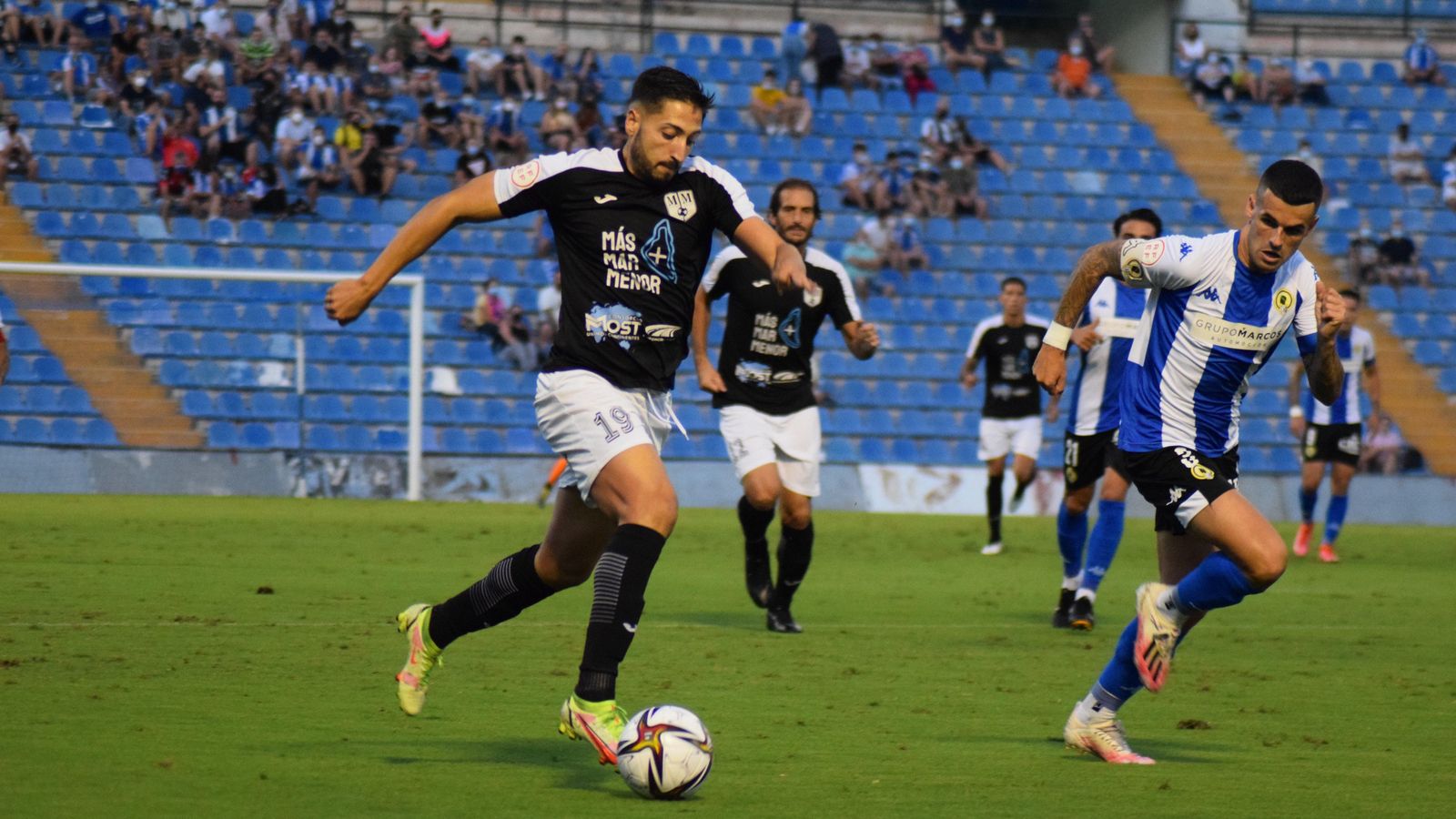 Un jugador del Mar Menor condueix la pilota davant la mirada d'un jugador de l'Hèrcules