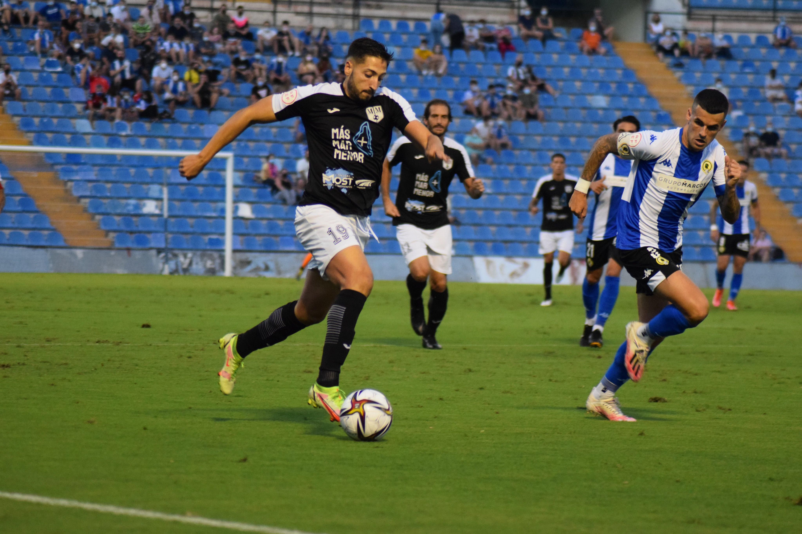 Un jugador del Mar Menor condueix la pilota amb la mirada fixa d'un jugador de l'Hèrcules Un jugador del Mar Menor condueix la pilota davant la mirada d'un jugador de l'Hèrcules