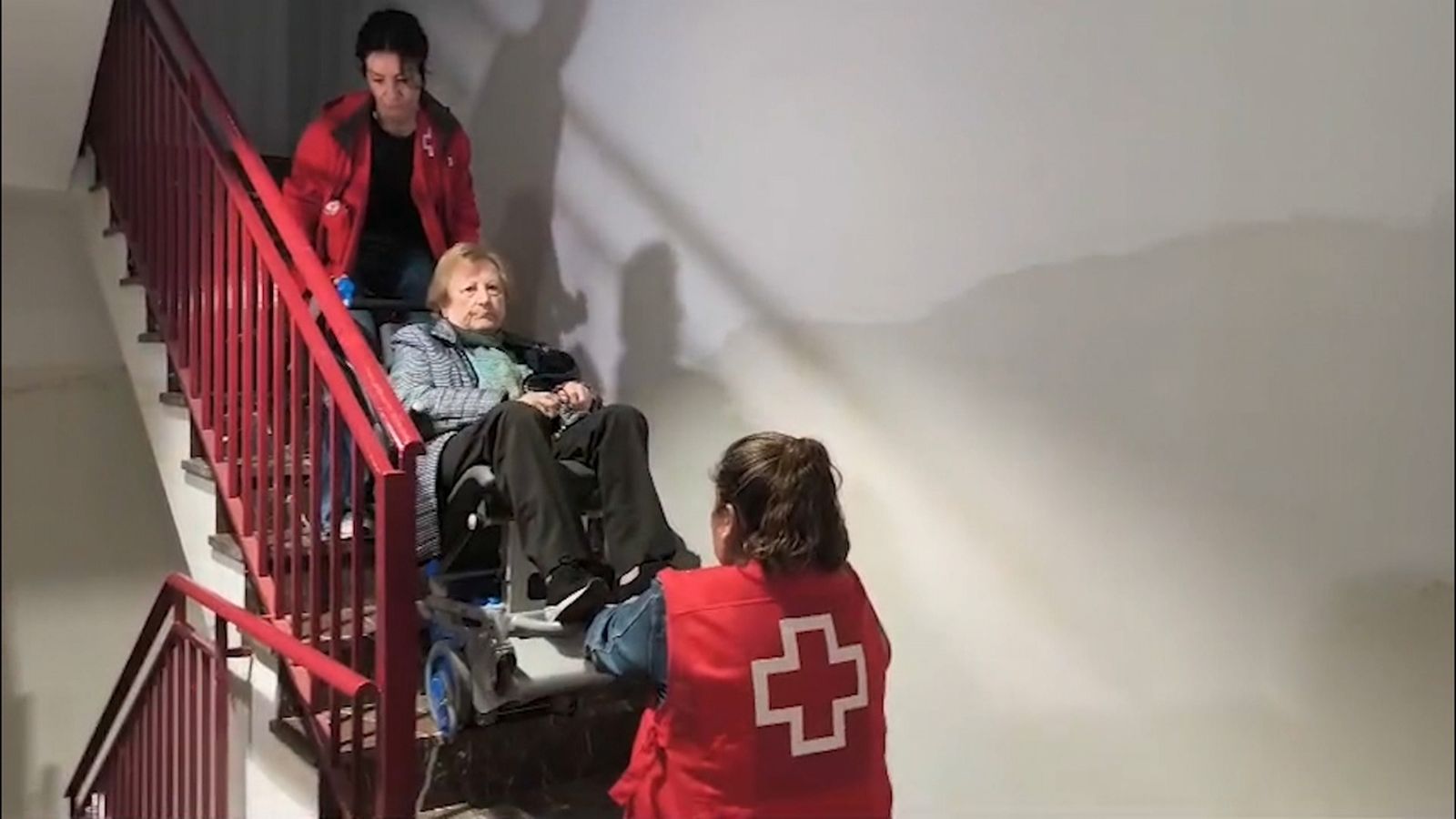 Dos tècniques de la Creu Roja ajuden una veïna a baixar les escales
