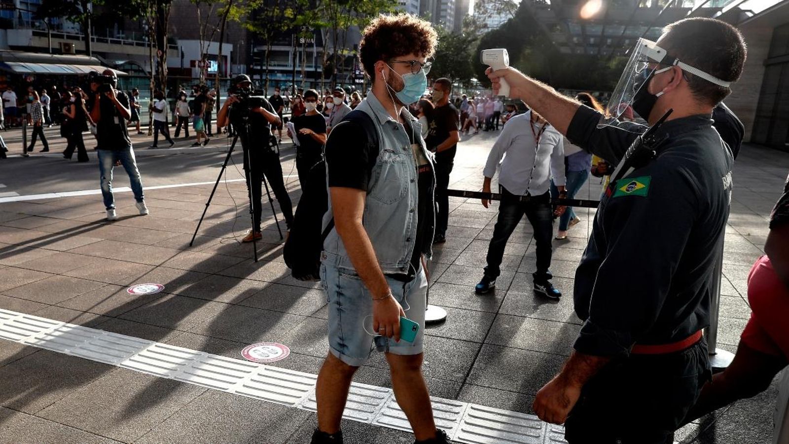 Un funcionari mesura la temperatura de la clientela abans d'entrar a un centre comercial, aquest dijous a Sao Paulo