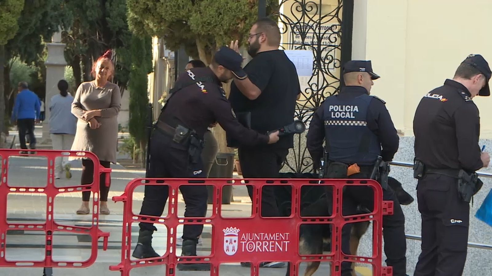 Un agent de policia passa un detector de metalls a un visitant del cementeri de Torrent que acudia a aquest espai a primera hora del matí