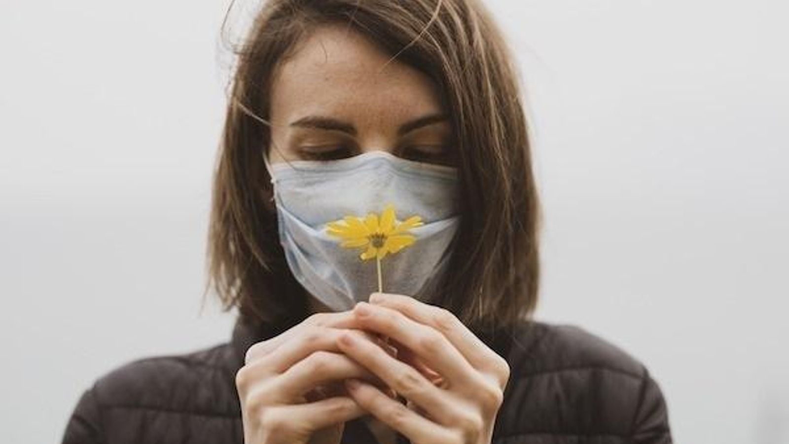 Imatge d'arxiu d'una dona amb mascareta, que intenta sentir l'olor d'una flor Imatge d'arxiu d'una dona amb mascareta intentant sentir l'olor d'una flor