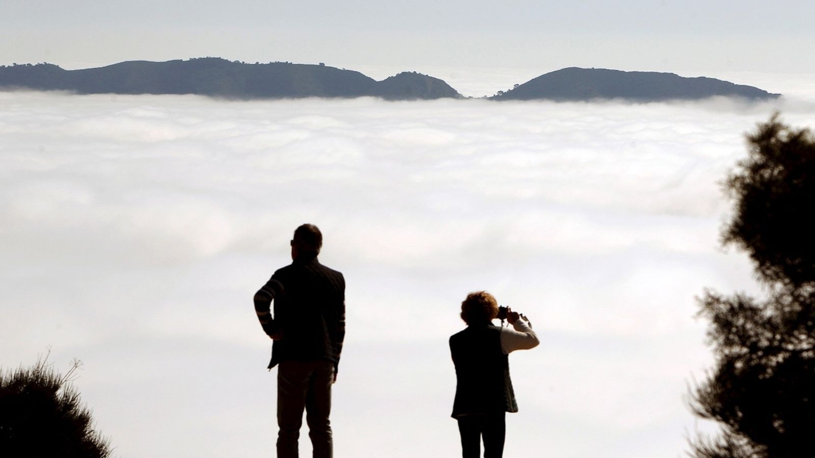 Dues persones contemplen des de la Serra Gelada la densa boira que cobreix Benidorm