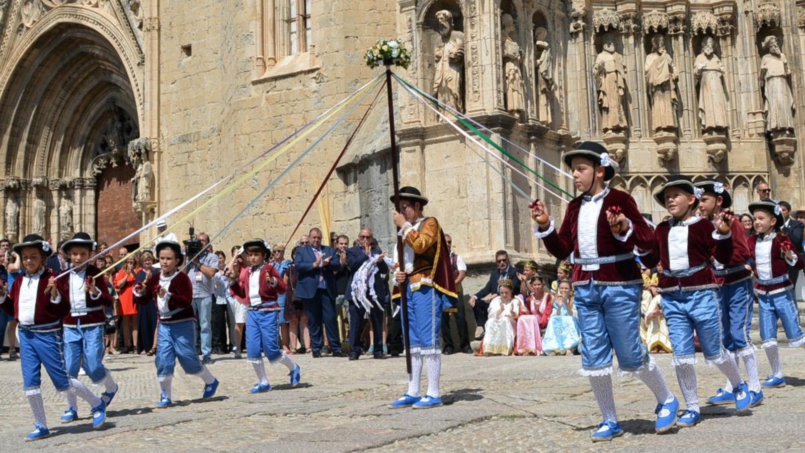 Xiquets dansen al voltant d'un pal de cinta de colors, teixint i desfent les cintes
