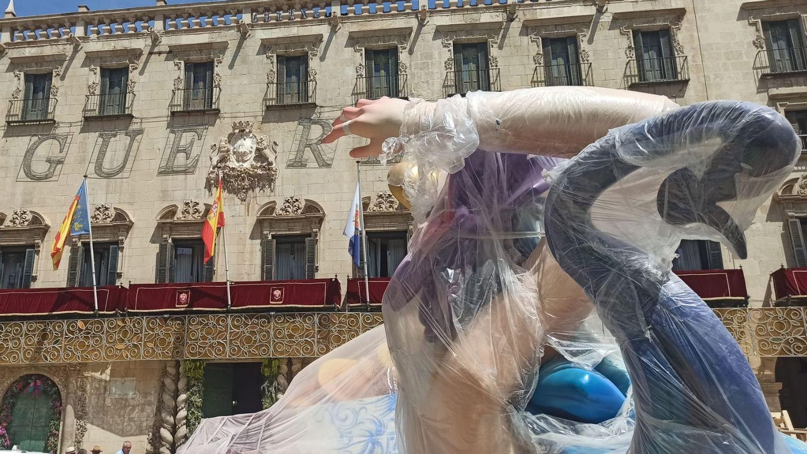 El remat del monument que ha fet Pedro Espadero espera, tapat amb plàstics, front a l'Ajuntament que les grues el puguen muntar