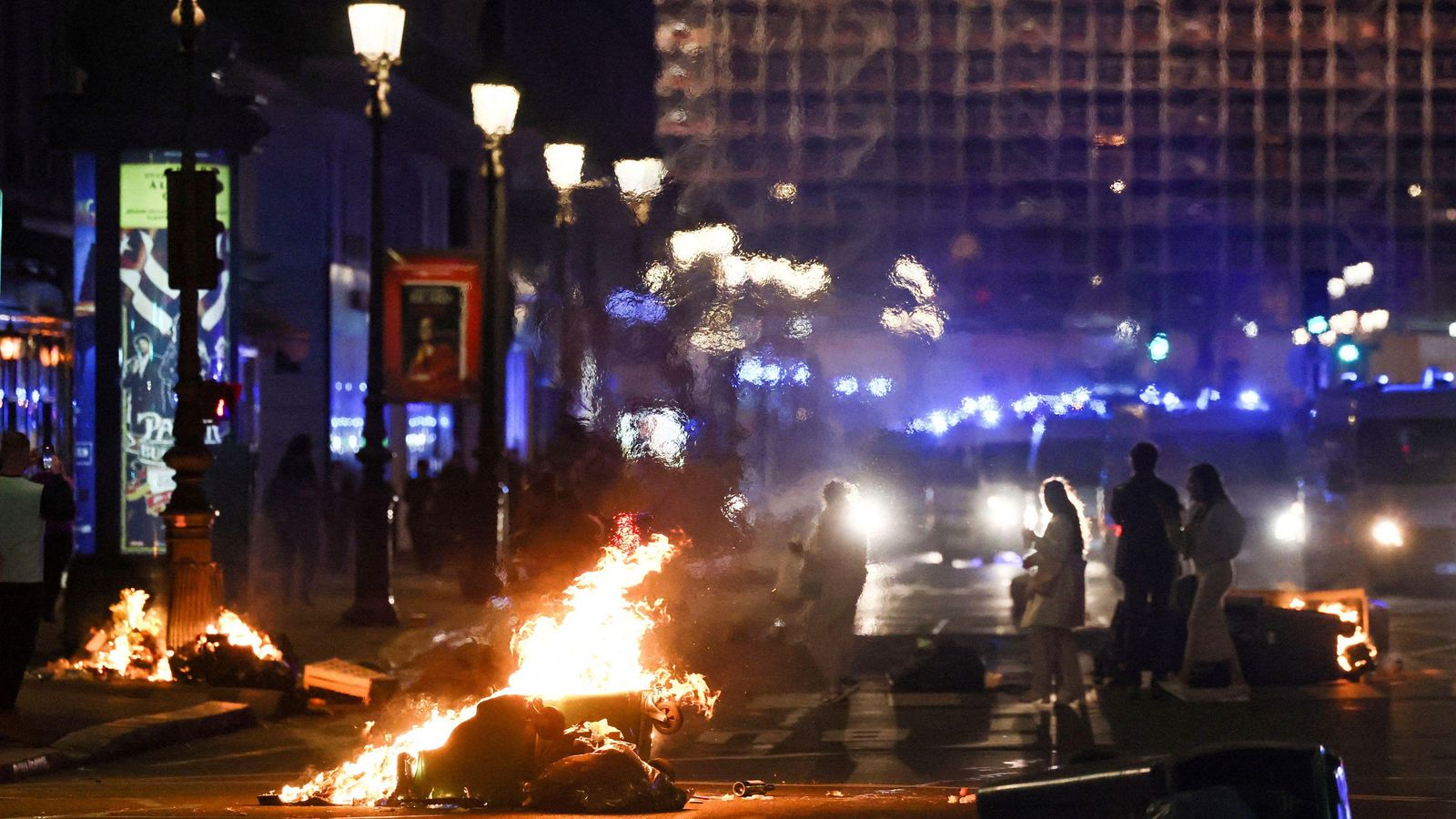 Els vianants passen entre les fogueres de fem incendiades prop de l’Òpera Garnier, a París, enceses pels manifestants en fracassar les mocions de censura contra Macron