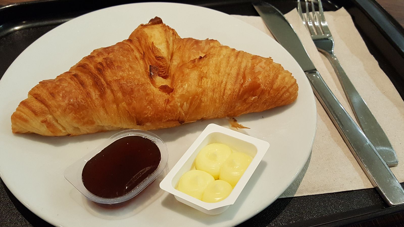 Monodosis de melmelada i mantega acompanyant un croissant en un bar