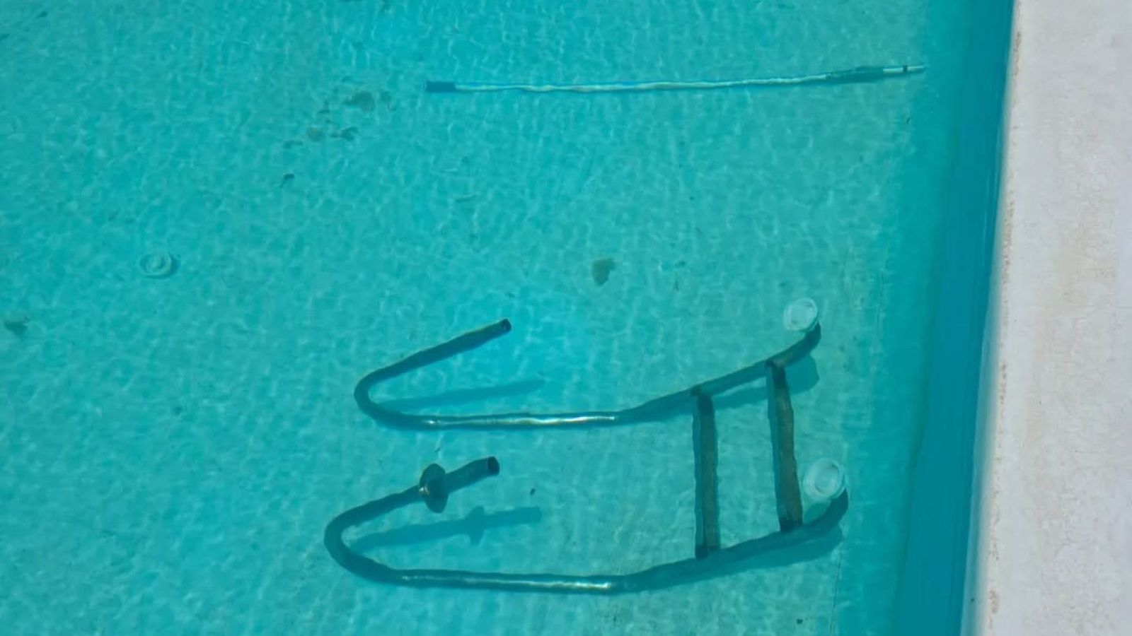 Una de les escales metàl·liques arrancades i part d'una dutxa trencada pels vàndals submergides en l'aigua