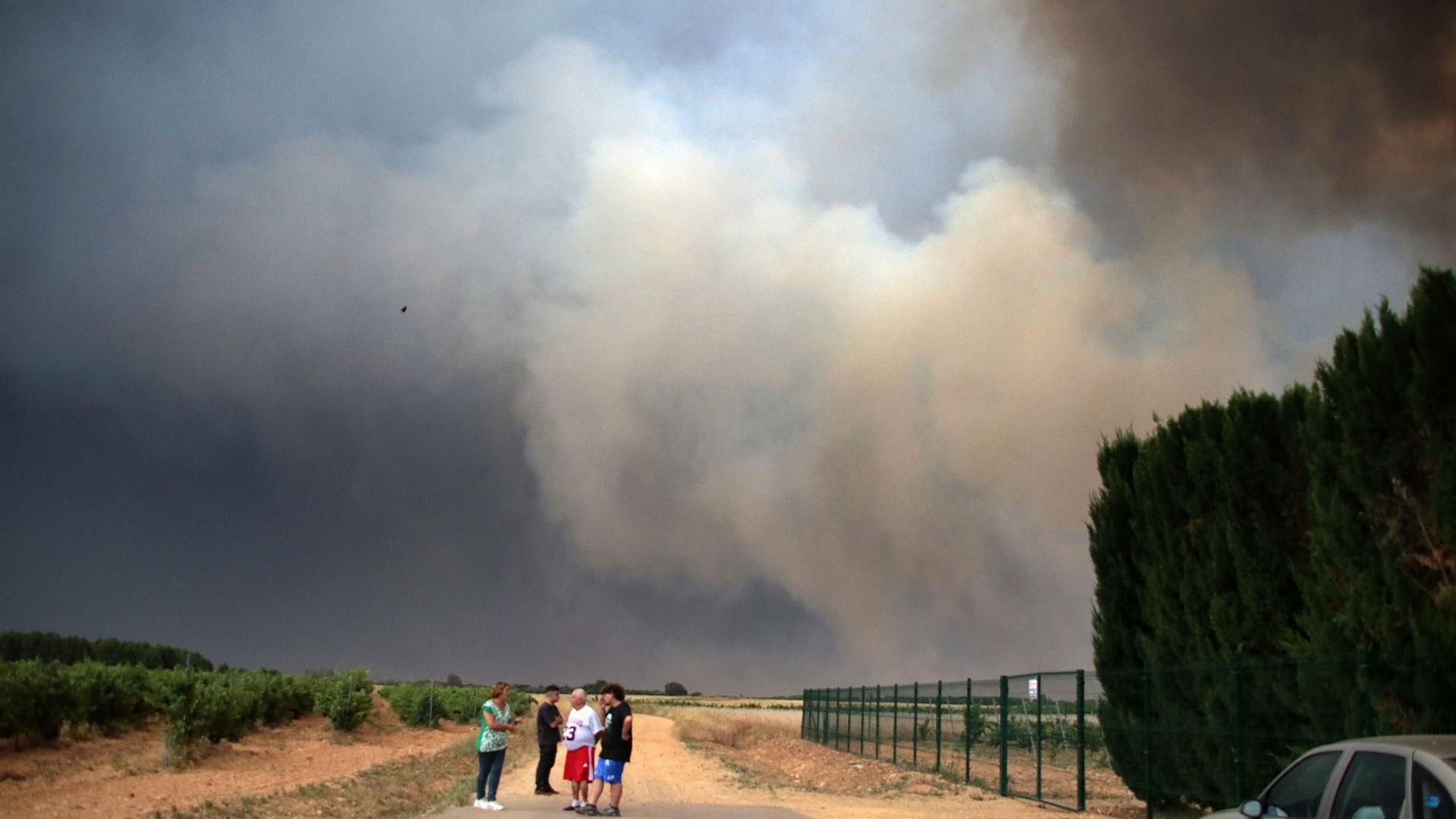 Diversos veïns conversen davant la imponent fumeguera de l’incendi que es va originar a Molezuelas de la Carballeda (Zamora)