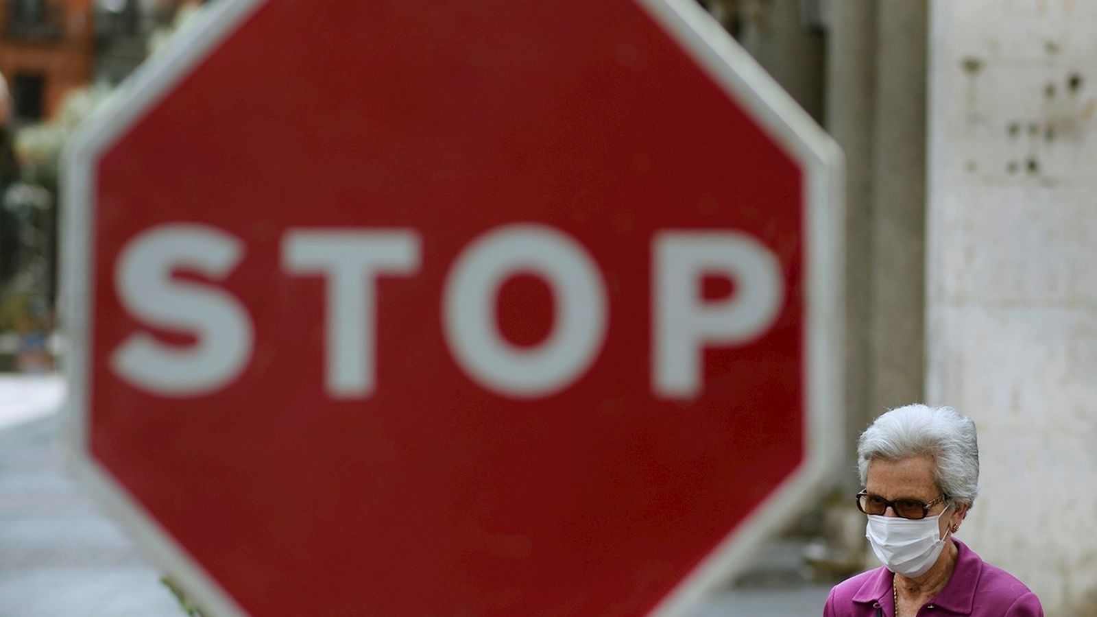 Una dona camina pel carrer amb mascareta, amb un senyal d'STOP al fons