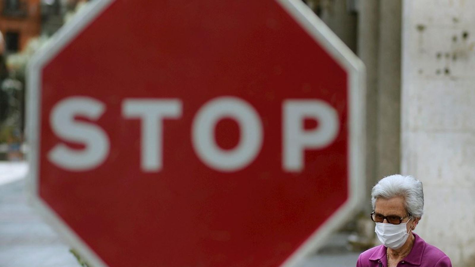Una dona camina pel carrer amb mascareta, amb un senyal d'STOP al fons