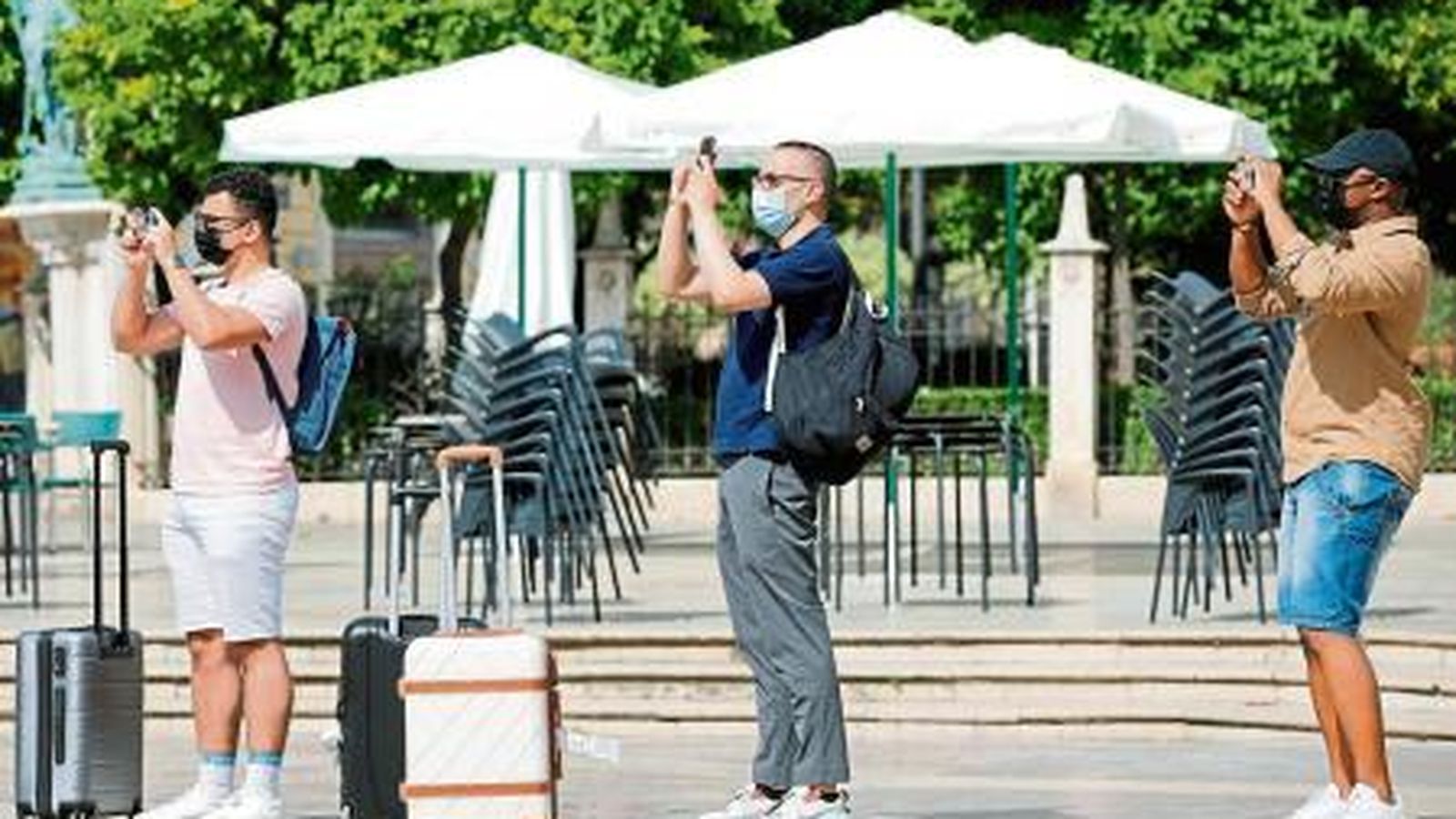 Tres turistes carregats amb les seues maletes realitzen una foto en la plaça de la Verge de València