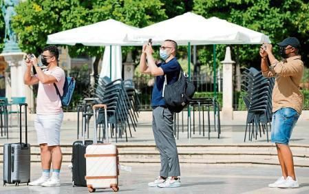 Tres turistes carregats amb les seues maletes realitzen una foto en la plaça de la Verge de València