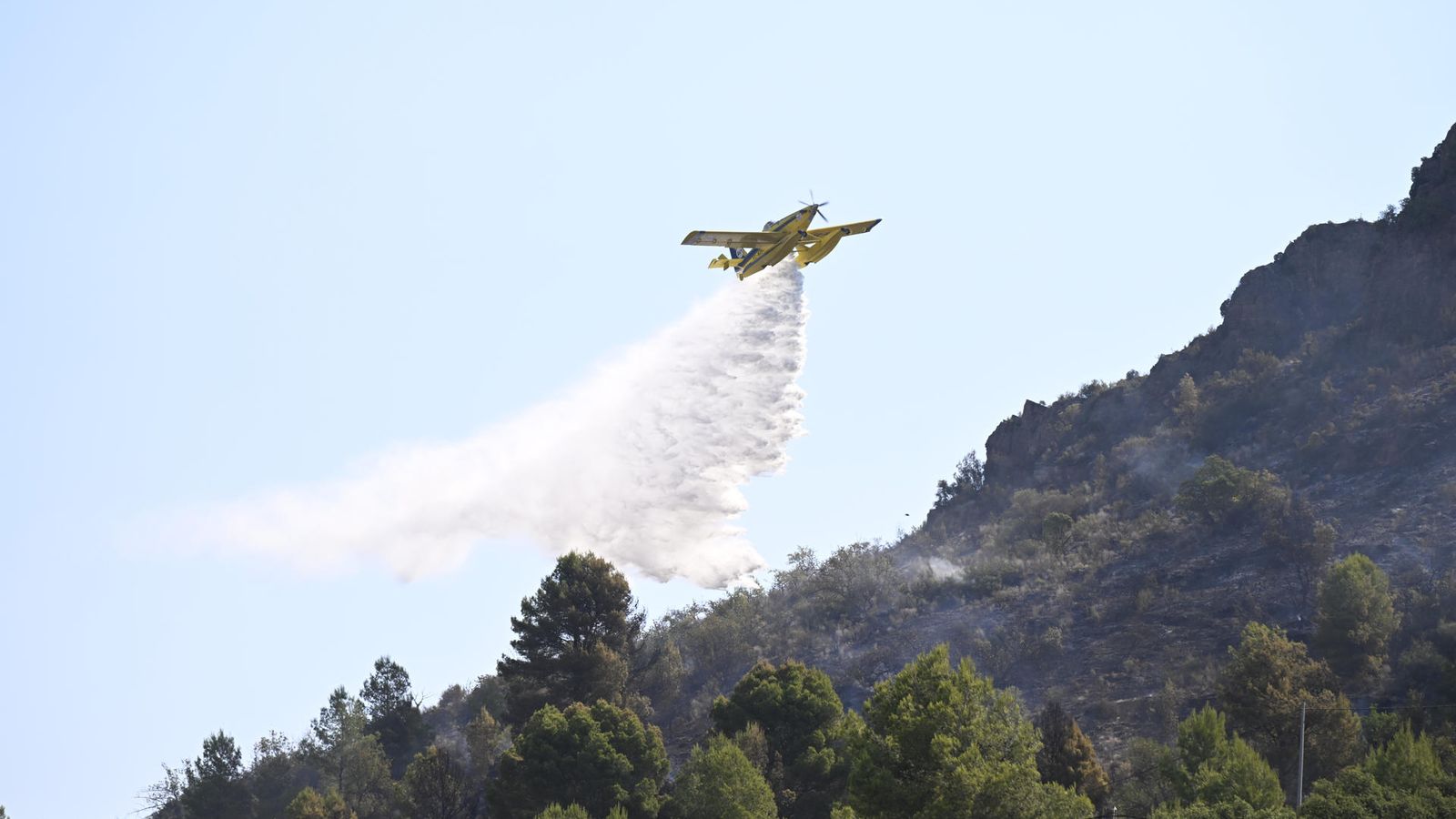 Un mitjà aeri llança una descàrrega d'aigua a la massa forestal afectada pel foc, este dilluns
