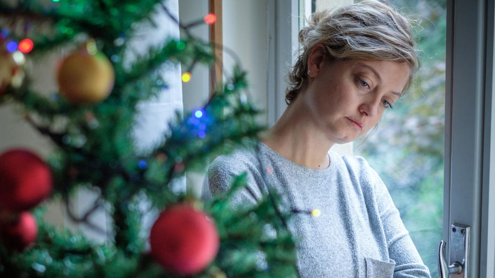 Una dona amb expressió trista al costat d'un arbre de Nadal