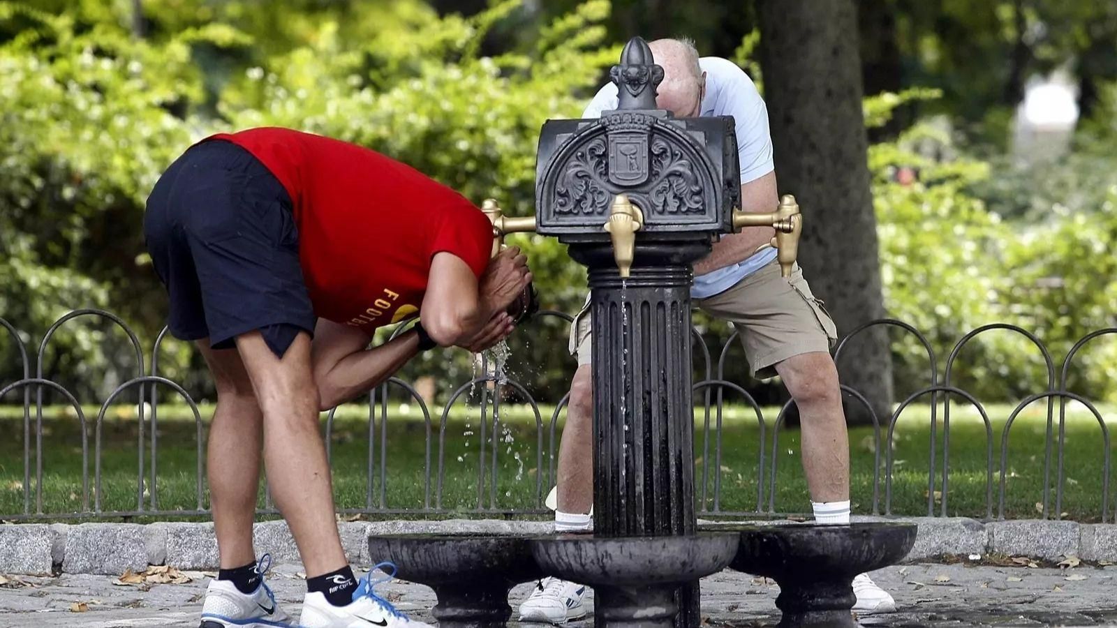 Dos persones lluiten contra la calor amb aigua d'una font