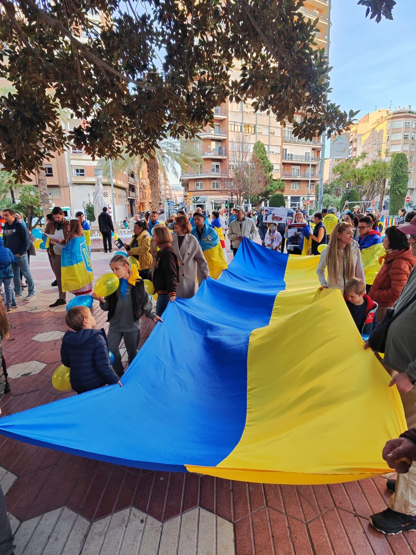 Un grup de persones estén una bandera d'Ucraïna a la plaça Maria Agustina de Castelló