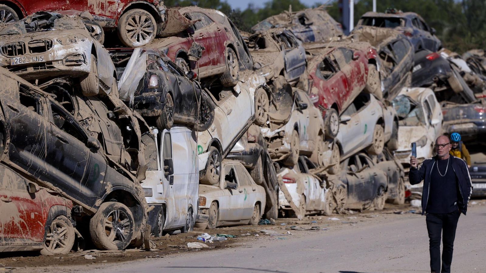 Un home camina al costat d'una campa amb cotxes apilats a Paiporta