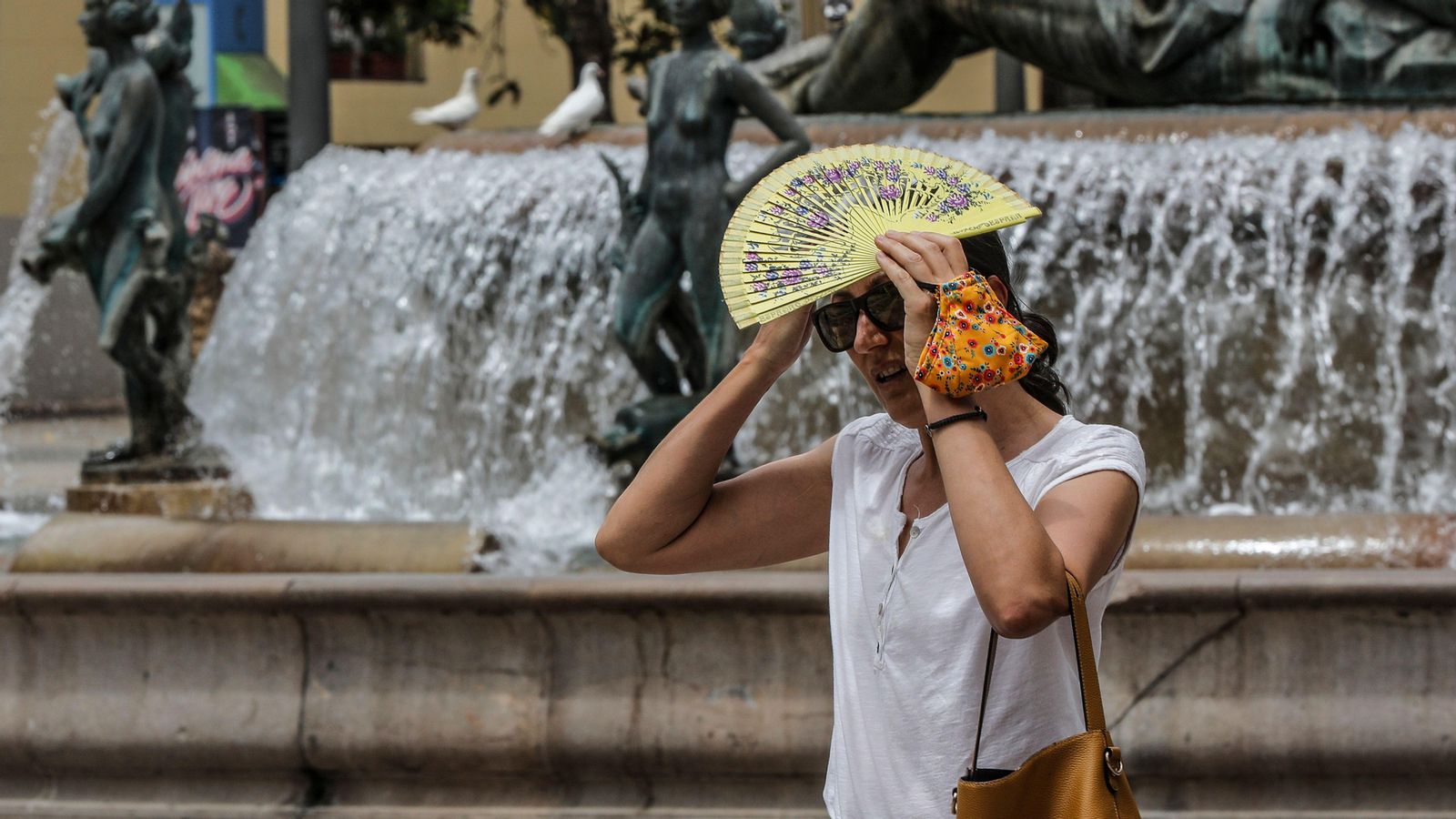Una dona es cobreix del sol amb el ventall a la Plaça de la Mare de Déu de València