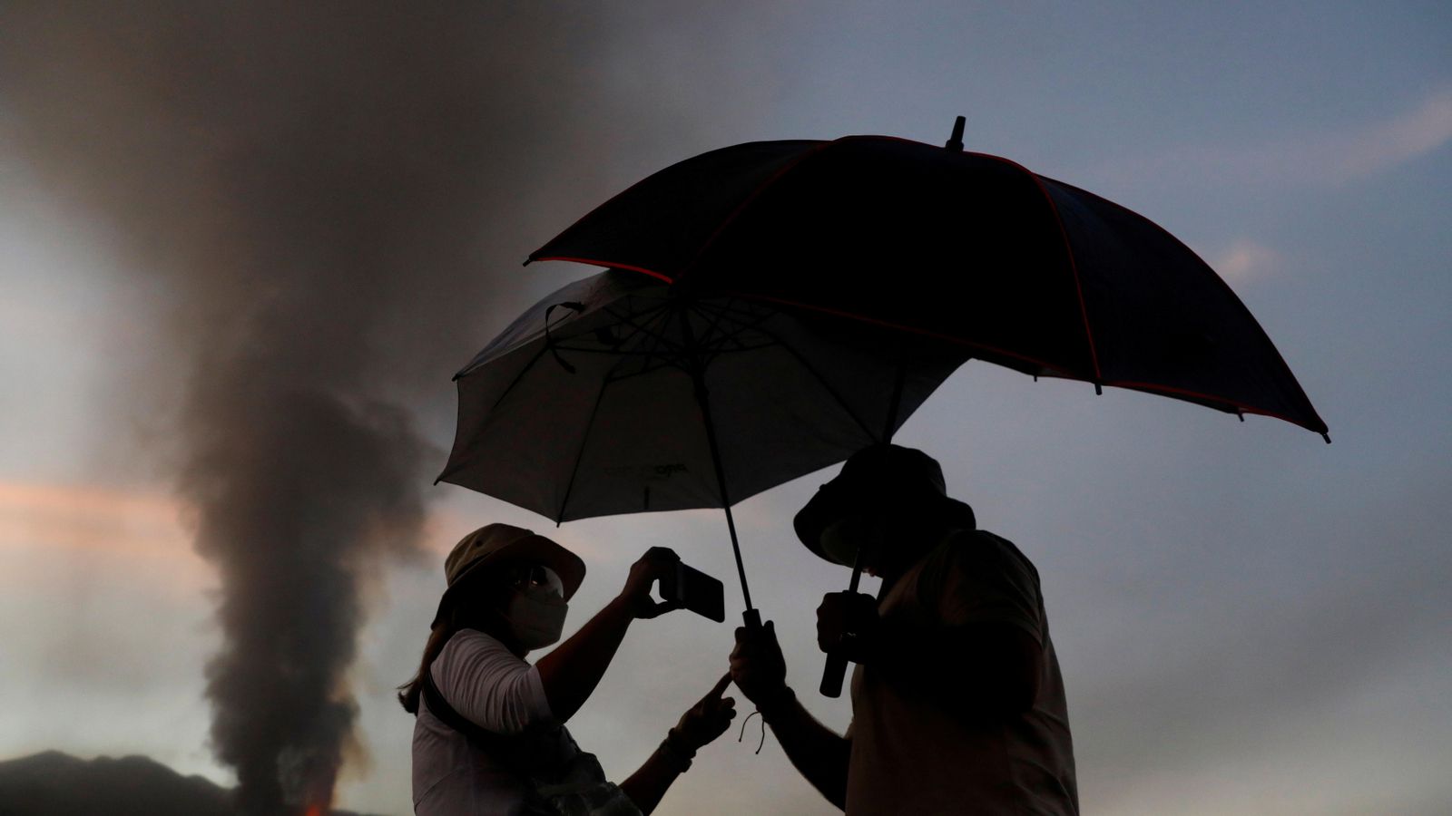 Dues persones es refugien amb paraigües de les cendres mentre observen l'erupció del volcà Cumbre Vieja