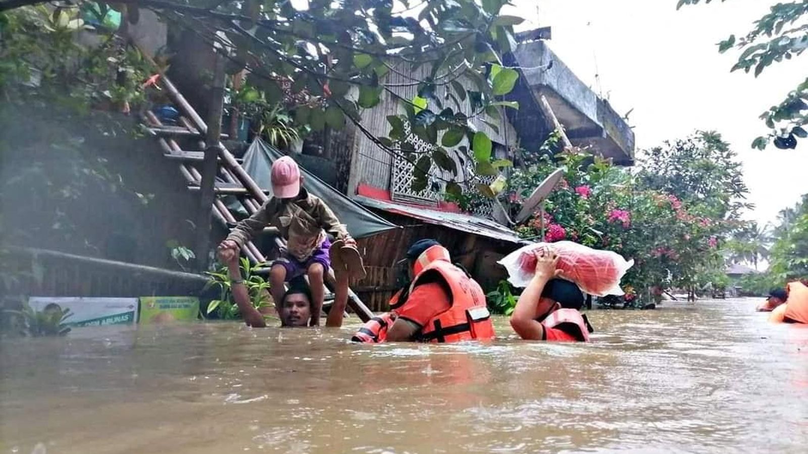 Un home porta un xiquet a l'esquena mentre caminen per una carretera negada juntament amb personal de rescat, a la província de Capiz