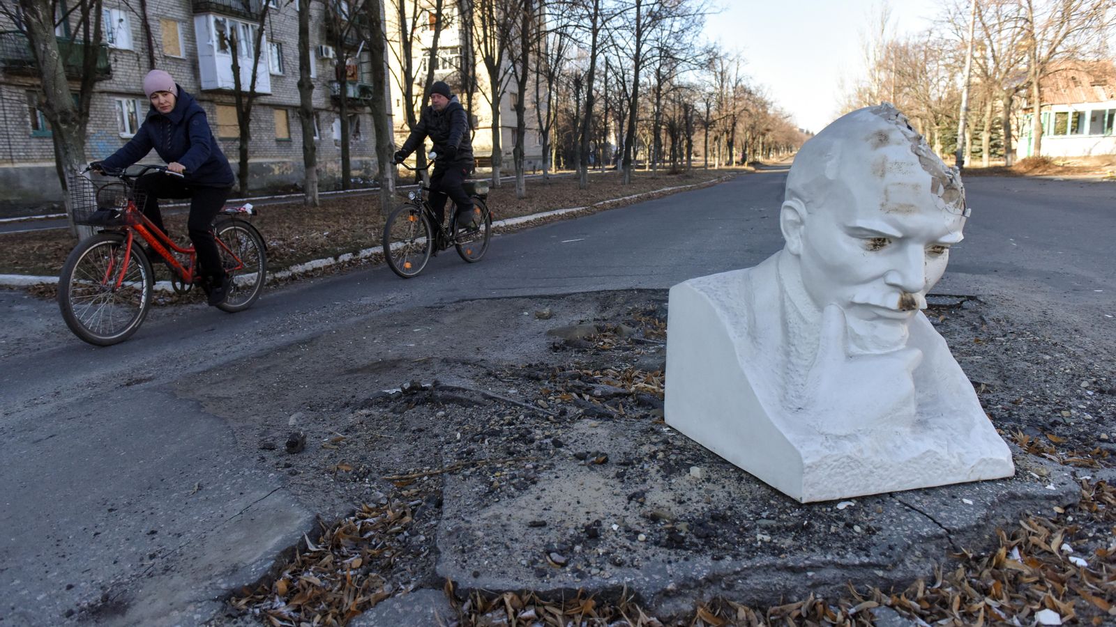 Ciclistes passen enfront del bust de Vladimir Lenin, que cobreix el cràter dels bombardejos a la regió de Lyman, Donetsk, en l'est d'Ucraïna