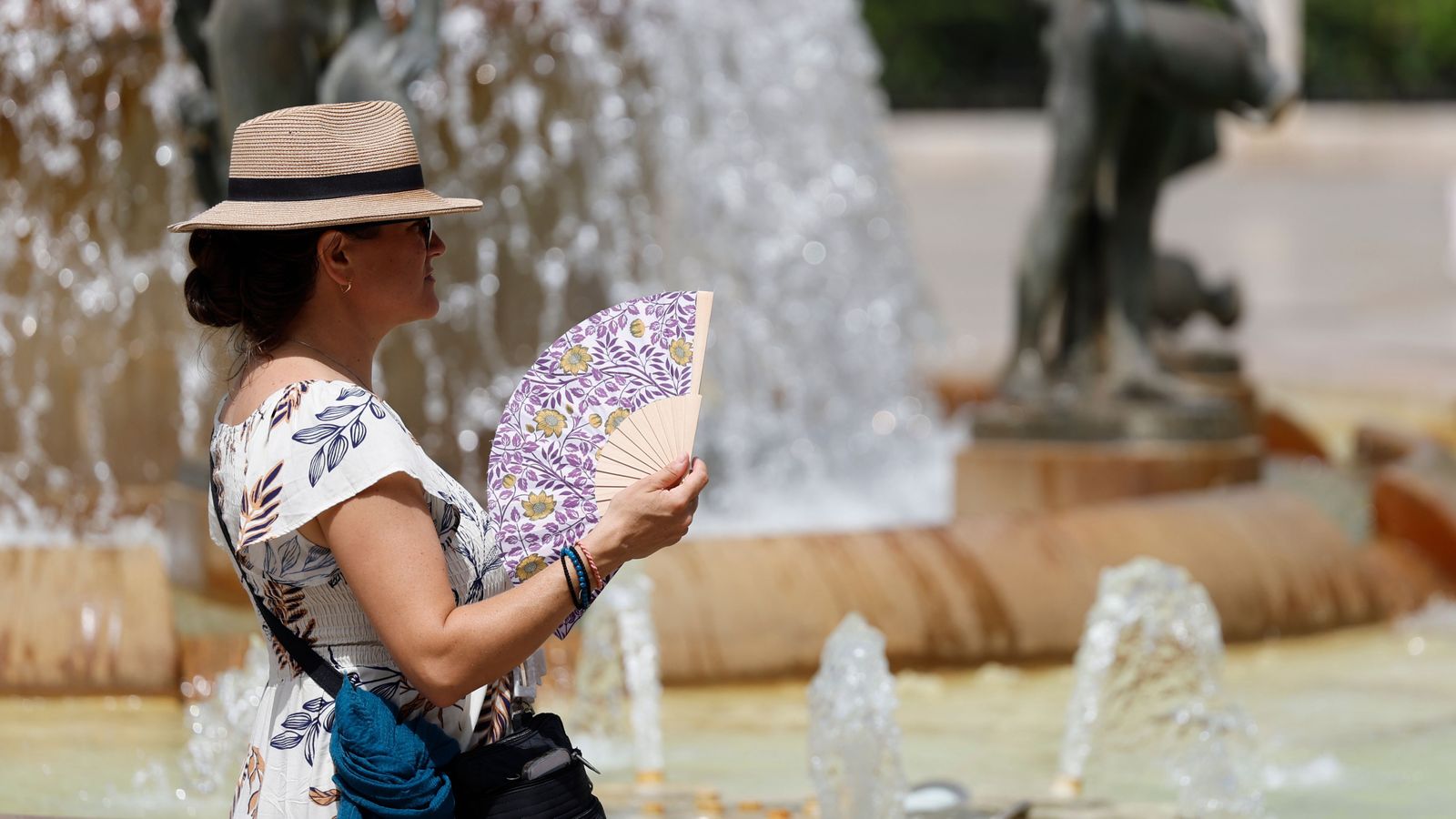 Una dona amb barret i ventall per a protegir-se de la calor