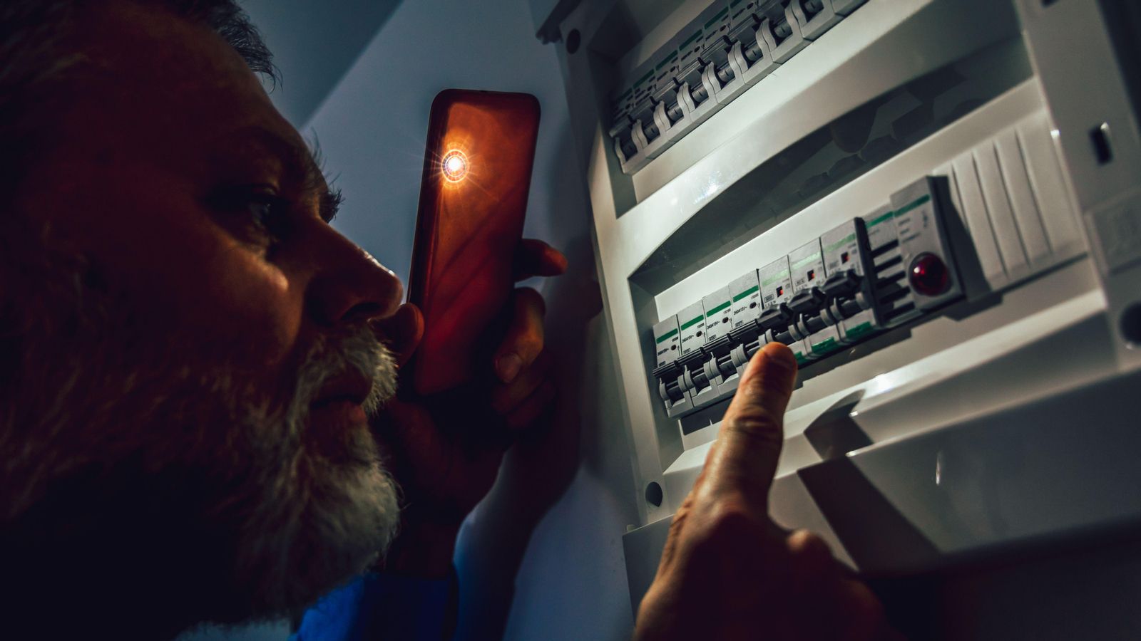 Un home il·lumina amb el mòbil el quadre elèctric de la seua casa