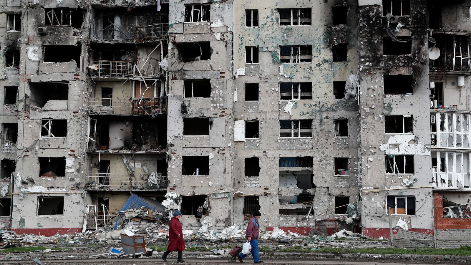 Dos veïns caminen al costat de les restes d'un edifici residencial de Mariúpol