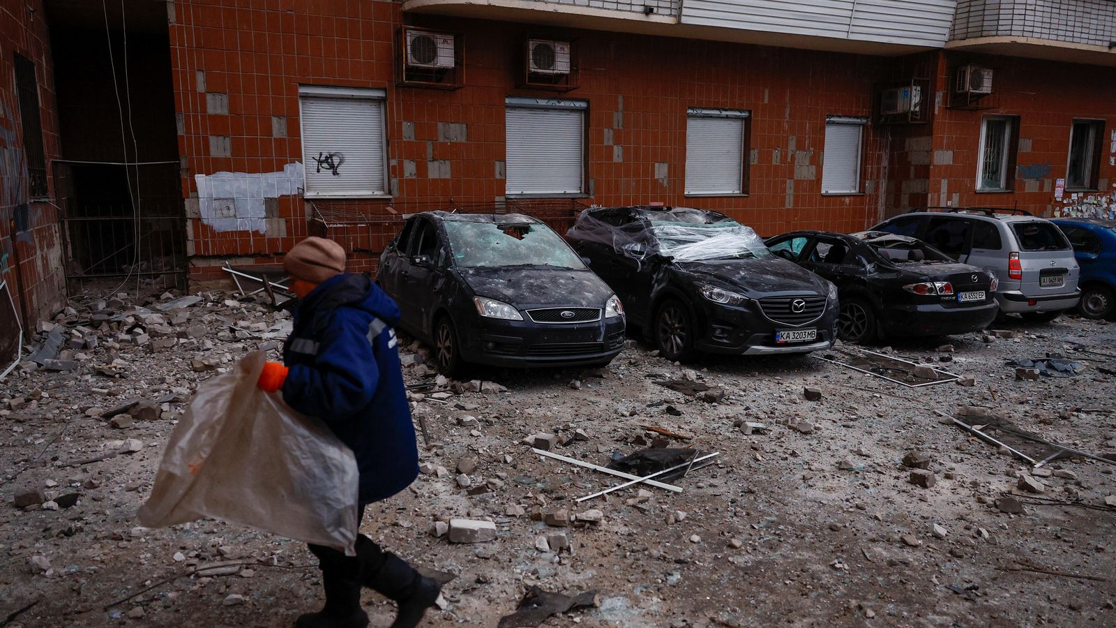 Un treballador municipal camina al costat d'automòbils danyats durant un atac amb drons russos a Kíiv, Ucraïna