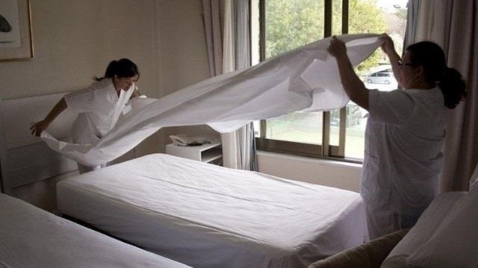 Dos cambreres de pis fent el llit d'un establiment hoteler en una imatge d'arxiu