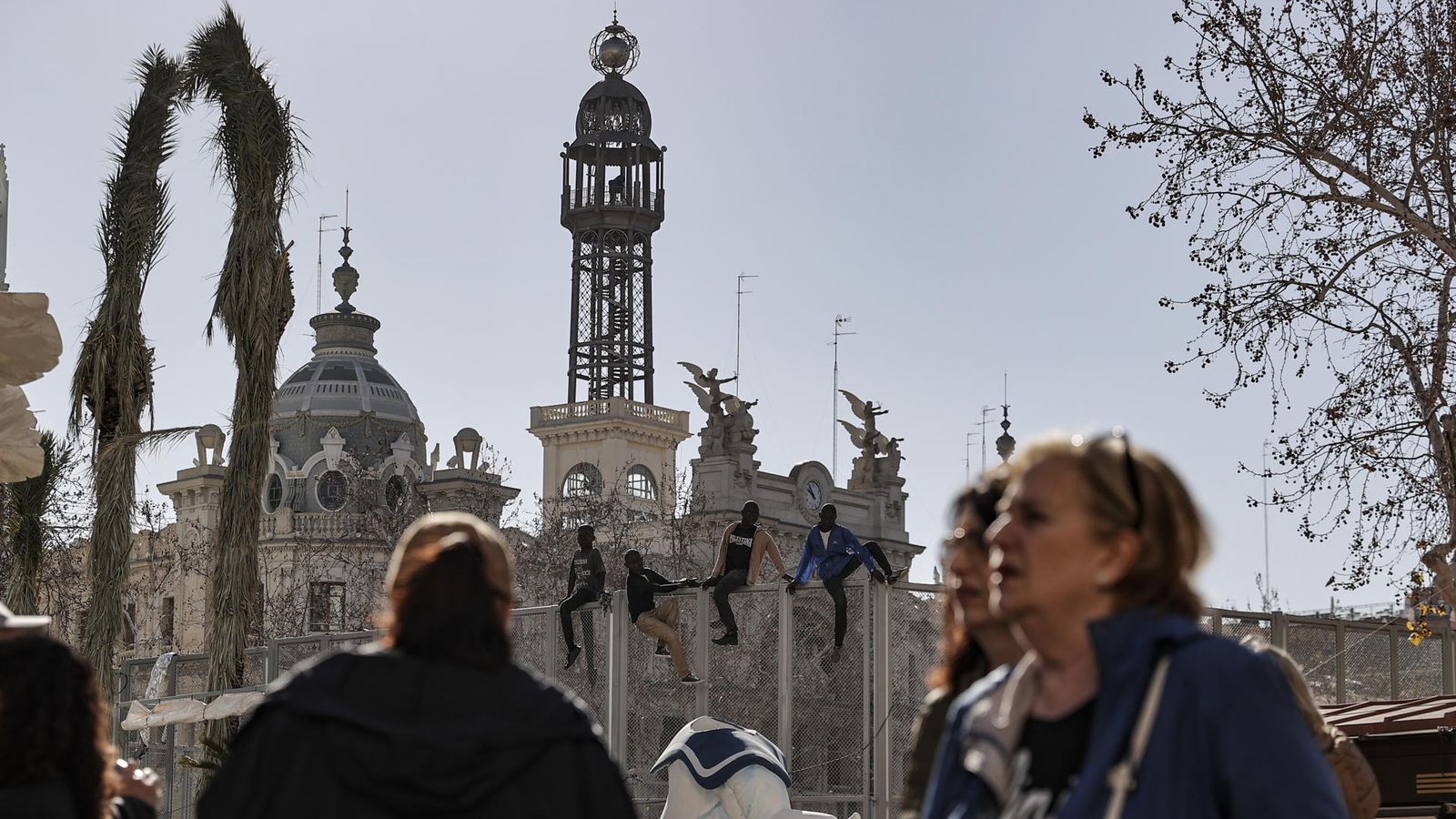 Vista de la plaça de l'Ajuntament de València, des d'on se disparen les mascletaes, amb quatre ninots de fons de la falla municipal que representen joves tractant de botar una tanca