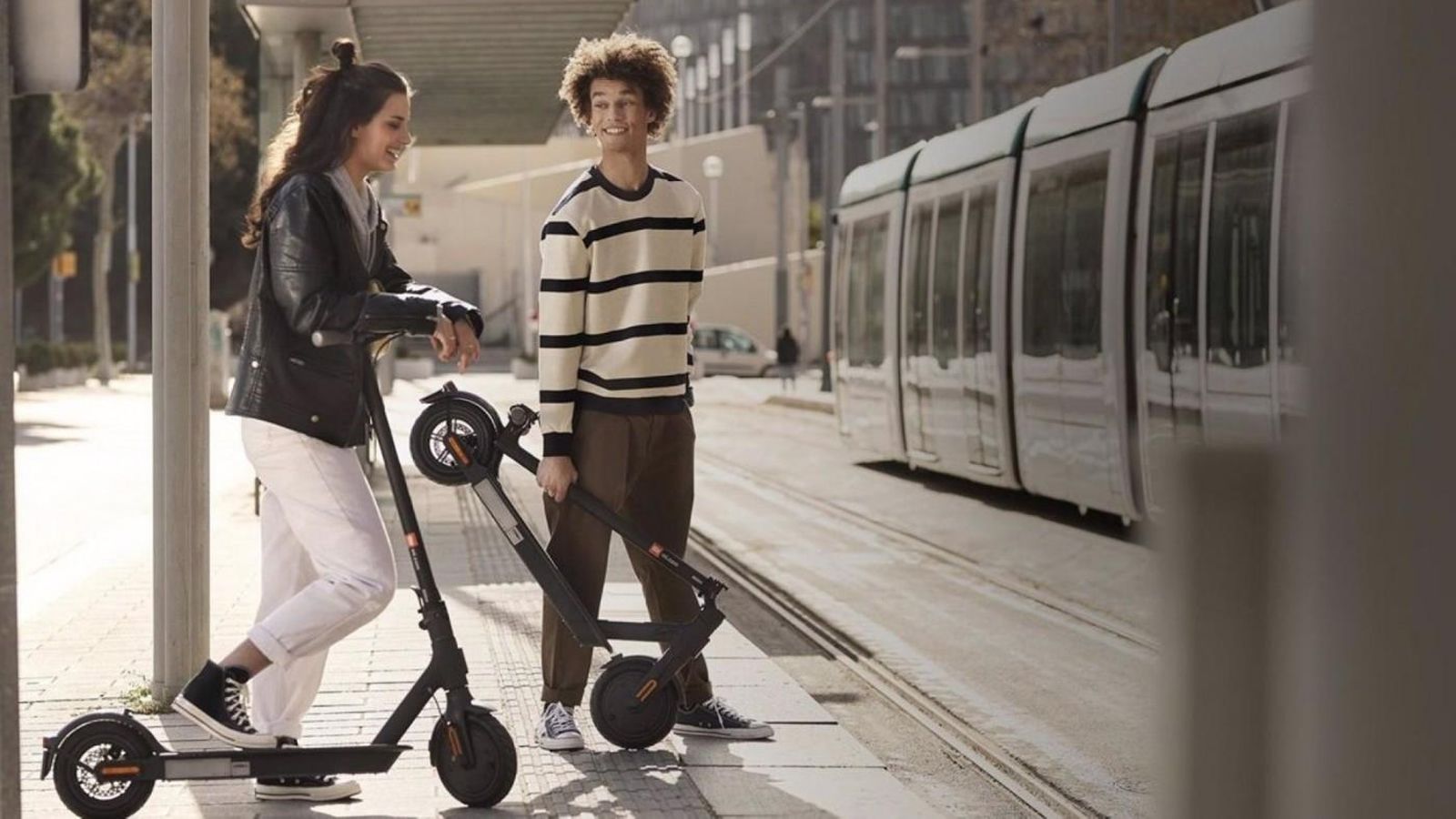Joves esperant l'arribada del tren amb els seus patinets en una imatge d'arxiu Joves esperant l'arribada del tren en els seus patinets en una imatge d'arxiu