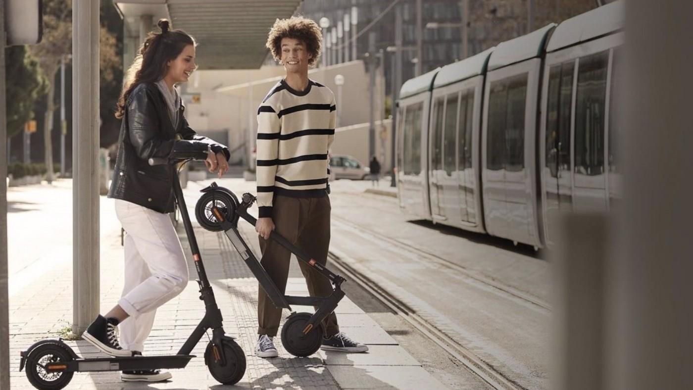 Joves esperant l'arribada del tren amb els seus patinets en una imatge d'arxiu Joves esperant l'arribada del tren en els seus patinets en una imatge d'arxiu