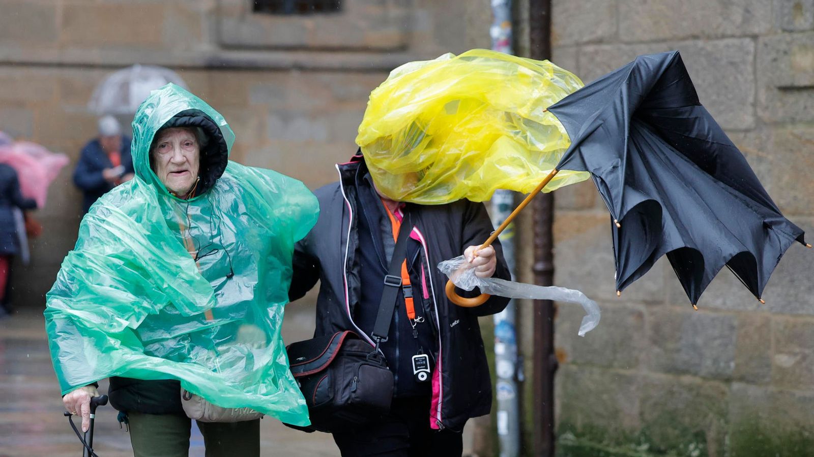 Dos persones caminen pel carrer amb un paraigua que s'envola pel vent