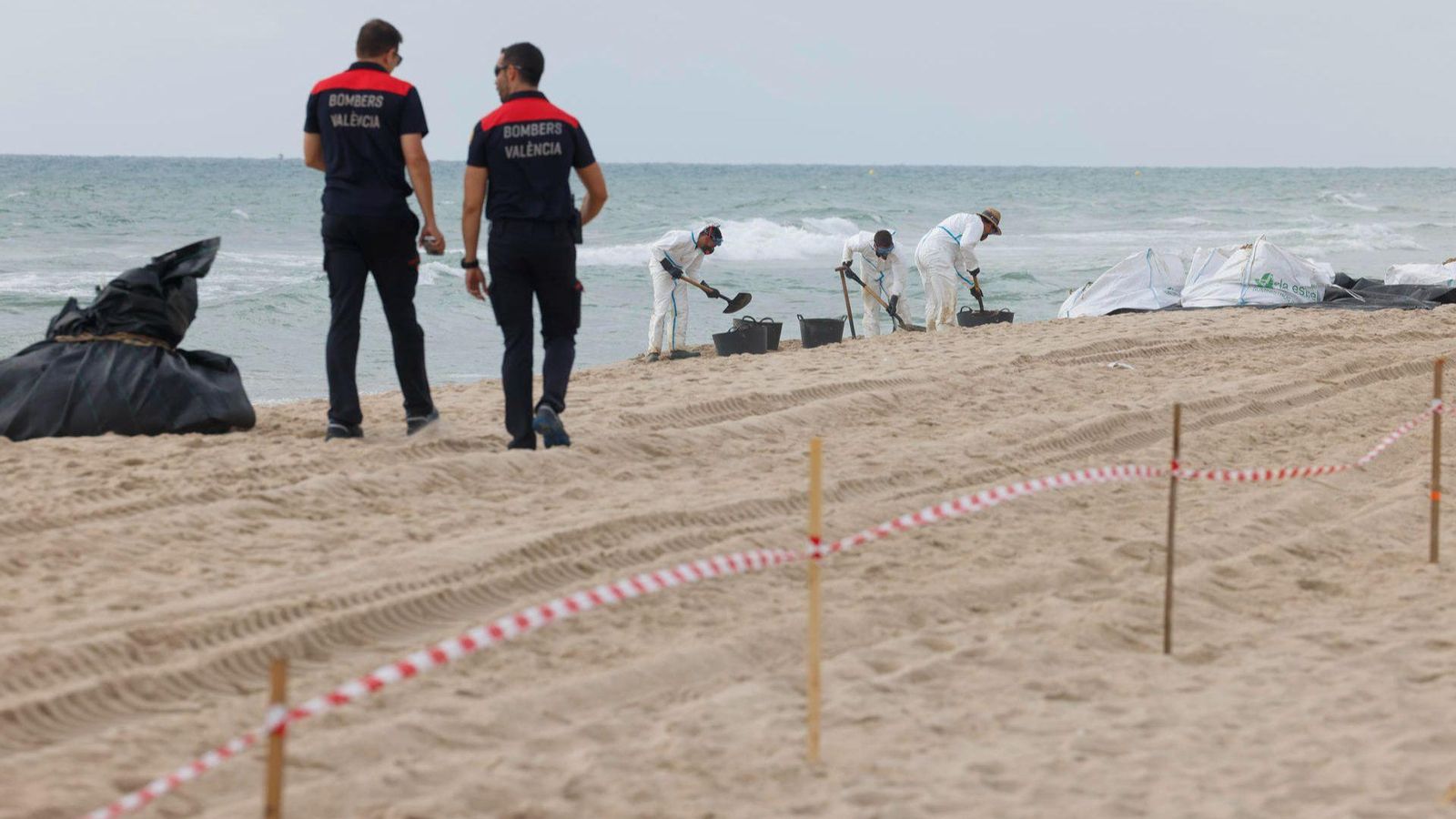 Dos bombers avancen entre els sacs i els cabassos amb les restes d'hidrocarburs que estan retirant-se de les tres platges afectades