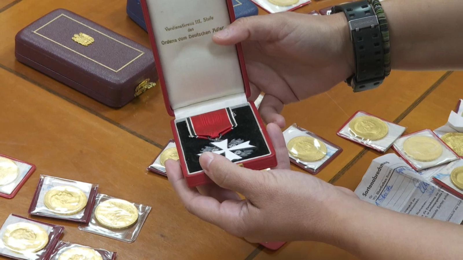 En primer pla, la insignía nazi que la Generalitat trau a subhasta, i al fons algunes de les monedes d'or