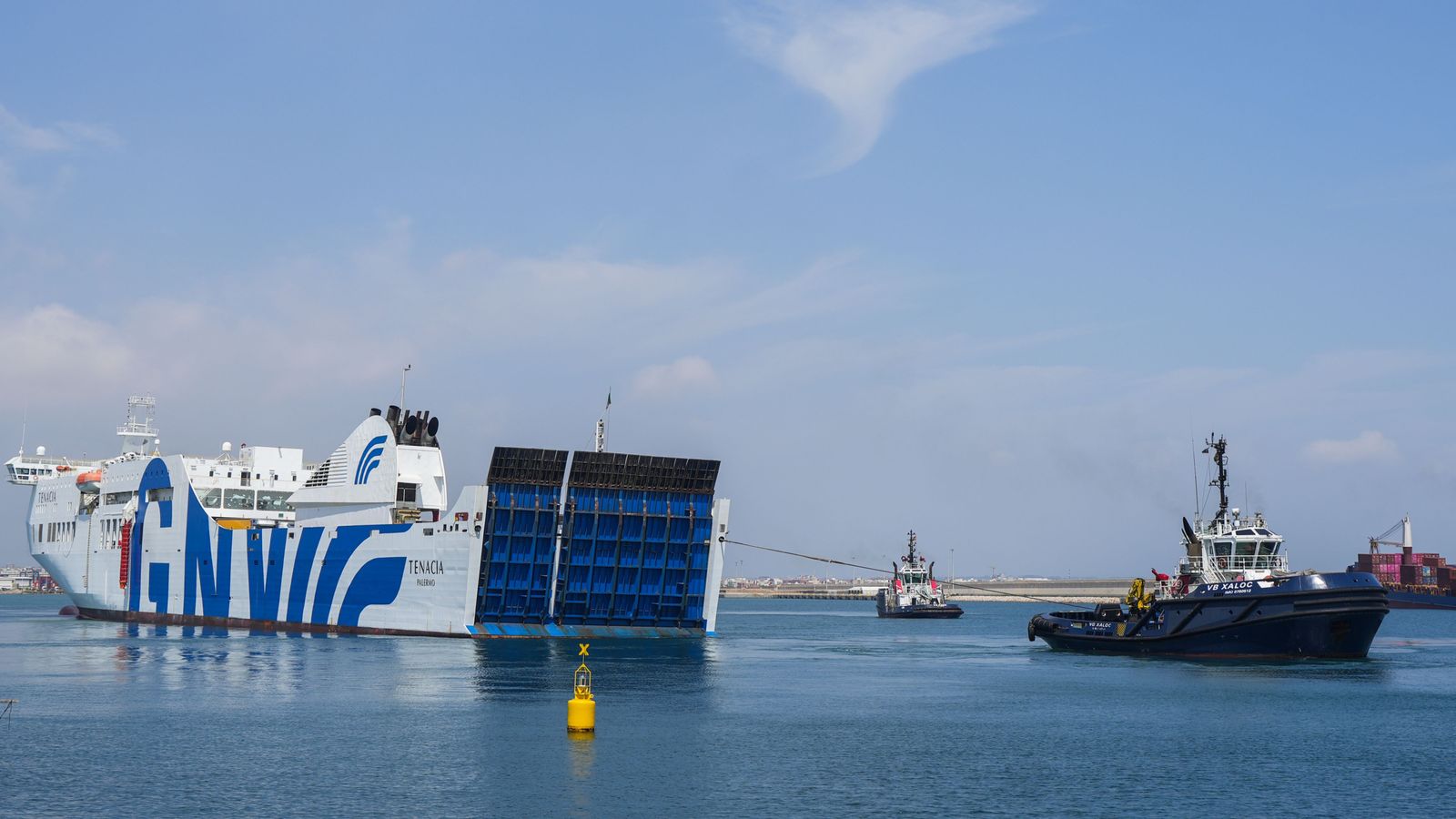 El vaixell incendiat, a l'esquerra de la imatge, entra a la bocana del port de València