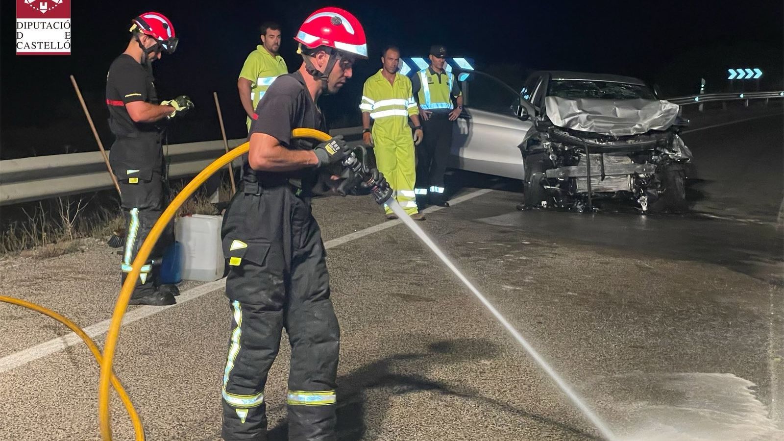 Dos bombers dels que van participar en les tasques de rescat netegen la calçada davant un dels vehicles implicats, que va quedar amb la part davantera desfeta