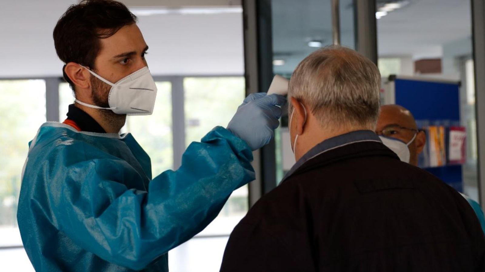 Personal sanitari pres la temperatura a una persona en l'entrada d'un centre de majors
