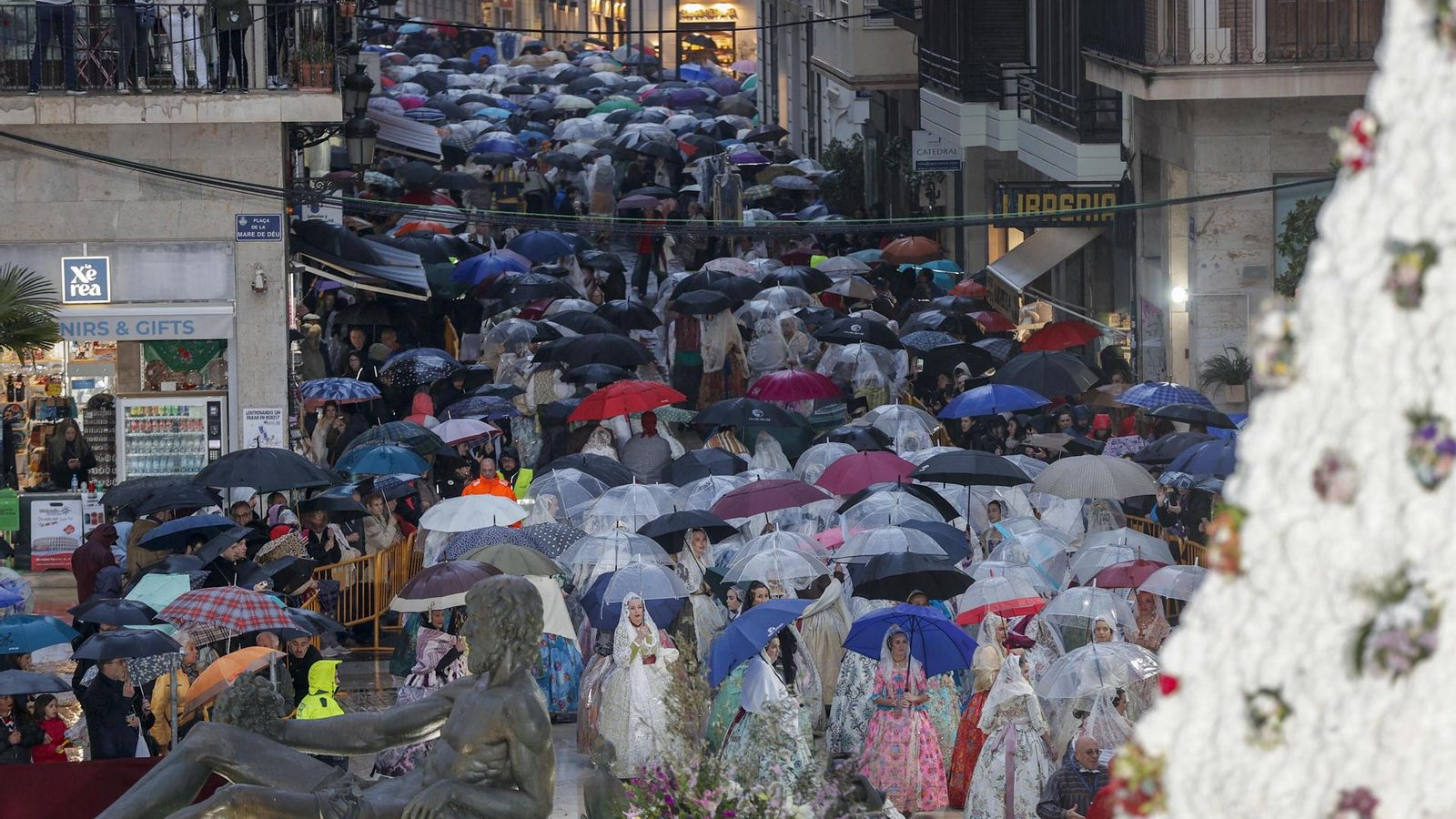 Arribada dels fallers i falleres amb paraigua i impermeable a la plaça de la Mare de Deu
