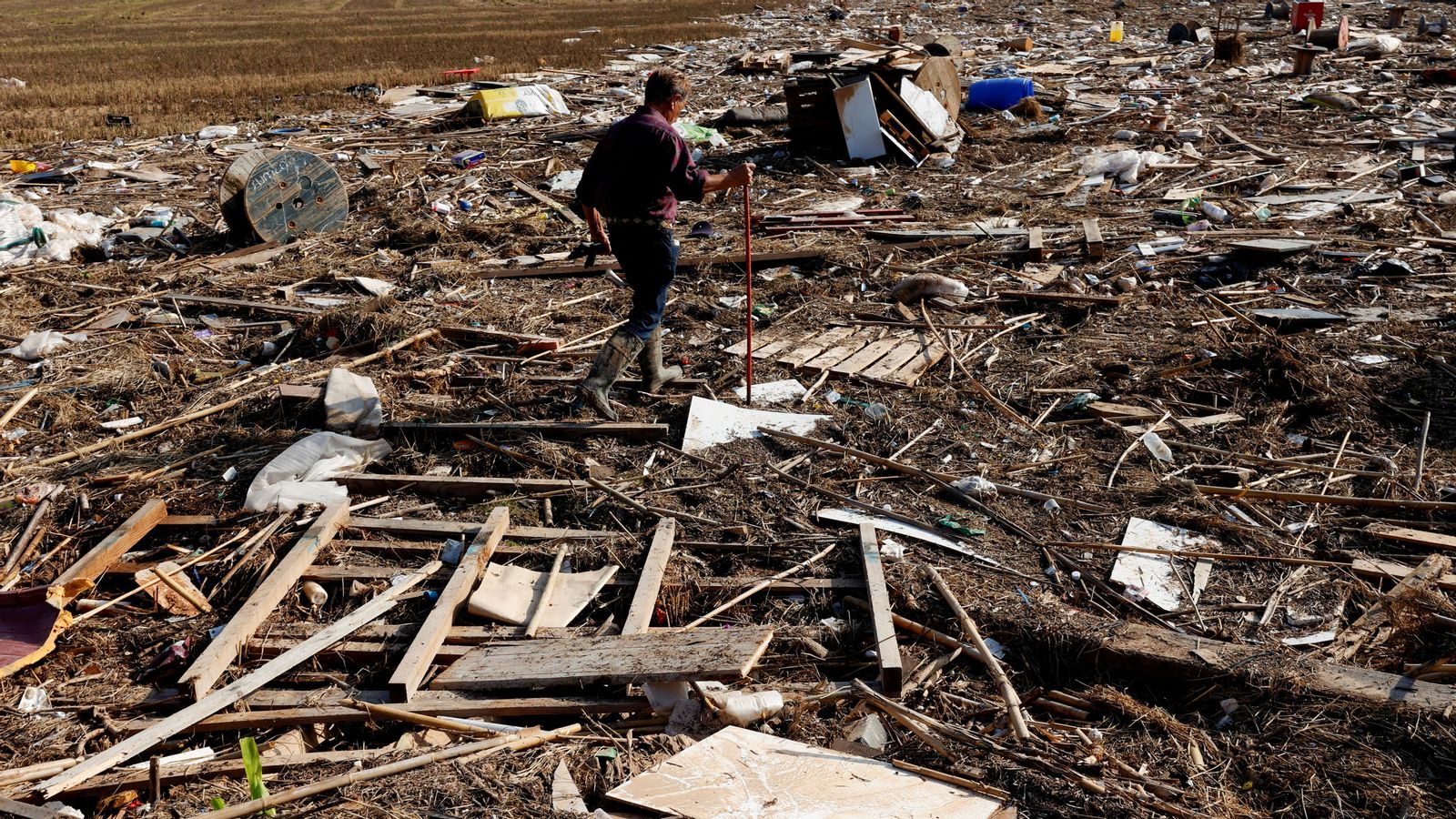 Un home camina sobre les restes de brutícia arrossegades per la DANA fins a l'horta