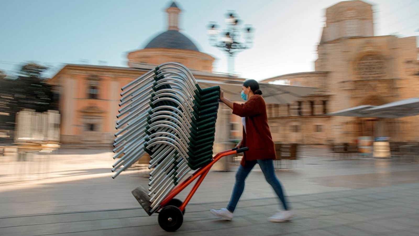 Una dona prepara les cadires d'una terrassa a la plaça de la Verge de València